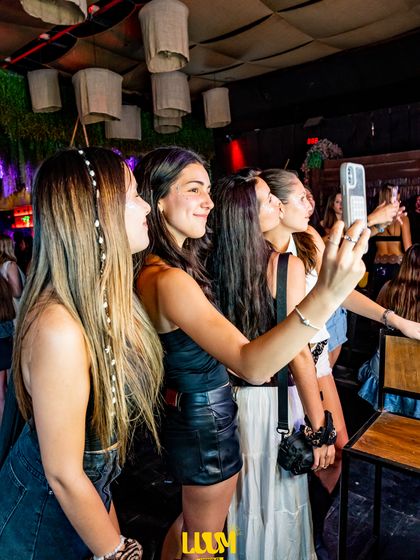 Dos amigas se toman una selfie con el teléfono en alto, en medio del salón.