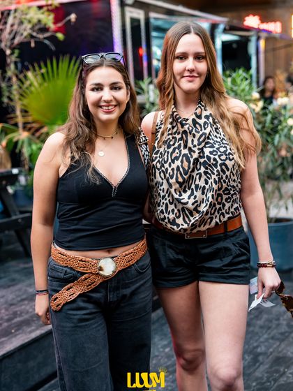 Dos amigas posan abrazadas entre las plantas colgantes de la terraza.