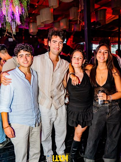 Cuatro amigos posan abrazados en el salón, dos de ellos de camisa clara.