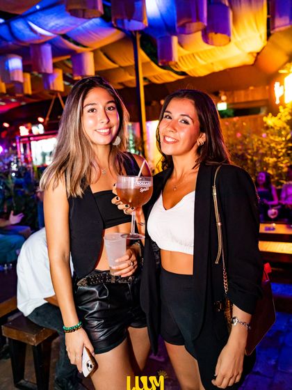 Dos amigas posan con sus copas bajo las lámparas colgantes del salón.