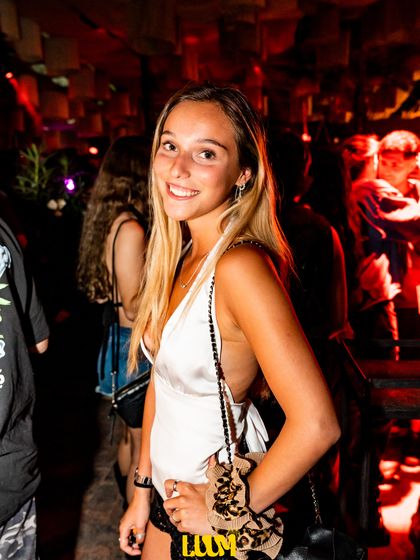Una joven con un bolso cruzado posa en el interior del local, con luz cálida.