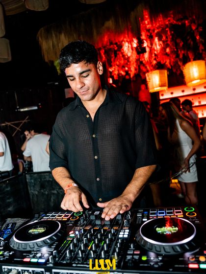 El DJ trabaja en la controladora bajo la luz roja, con las plantas del local detrás.