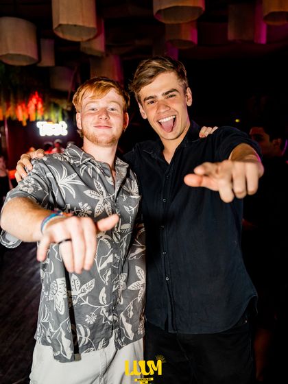 Dos amigos apuntan a la cámara entre risas, en medio de la fiesta.