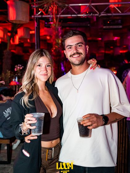 Una pareja con sus vasos posa abrazada bajo la luz roja del salón.