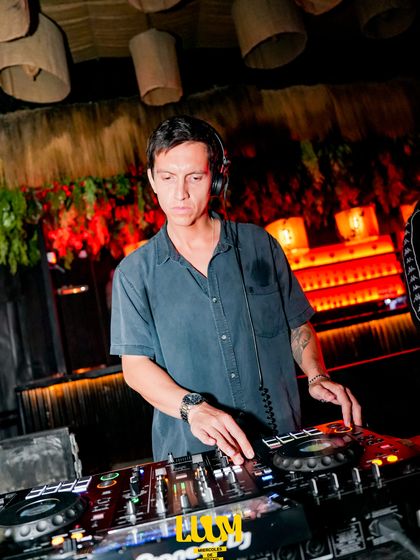 El DJ trabaja en la cabina con sus audífonos puestos, con el muro de bambú detrás.