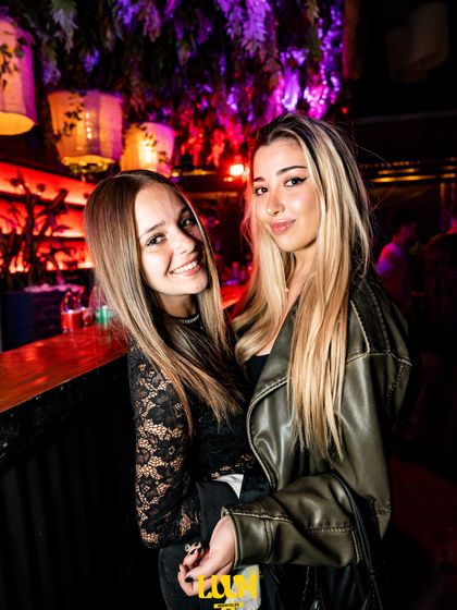 Dos amigas posan juntas bajo la luz violeta del salón.
