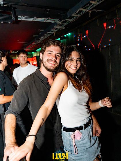 Una pareja baila abrazada en la pista, entre luces turquesa y rojas y gente alrededor.