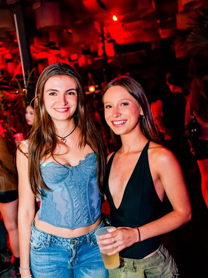 Dos amigas posan juntas con la luz roja del salón detrás.