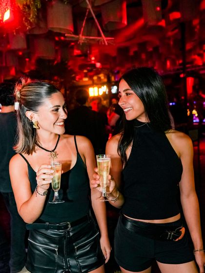 Dos amigas brindan con copas de champaña bajo la luz roja.