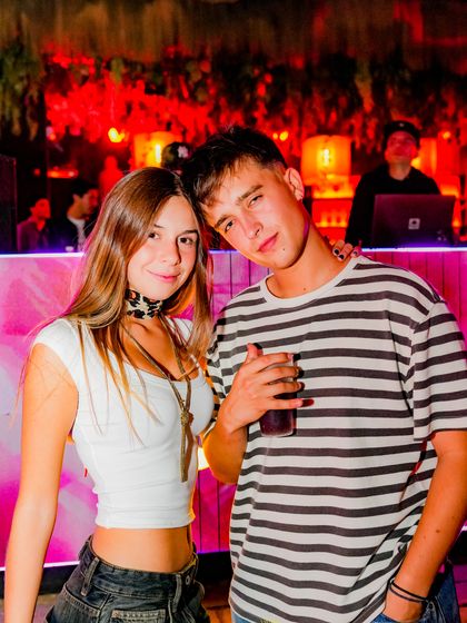 Una pareja posa frente a una pantalla rosada, con la cabina del DJ al fondo.