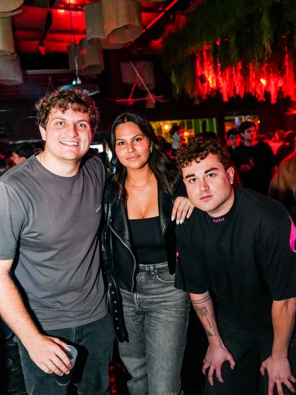 Tres amigos posan juntos en medio de la fiesta, con la gente detrás.