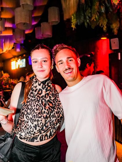 Una pareja posa abrazada bajo las lámparas de mimbre y la luz roja.