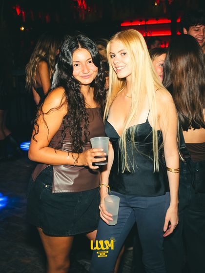 Dos amigas posan abrazadas en la penumbra del salón.
