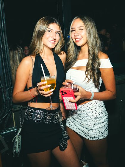 Dos amigas con sus tragos posan juntas en un rincón oscuro del local.